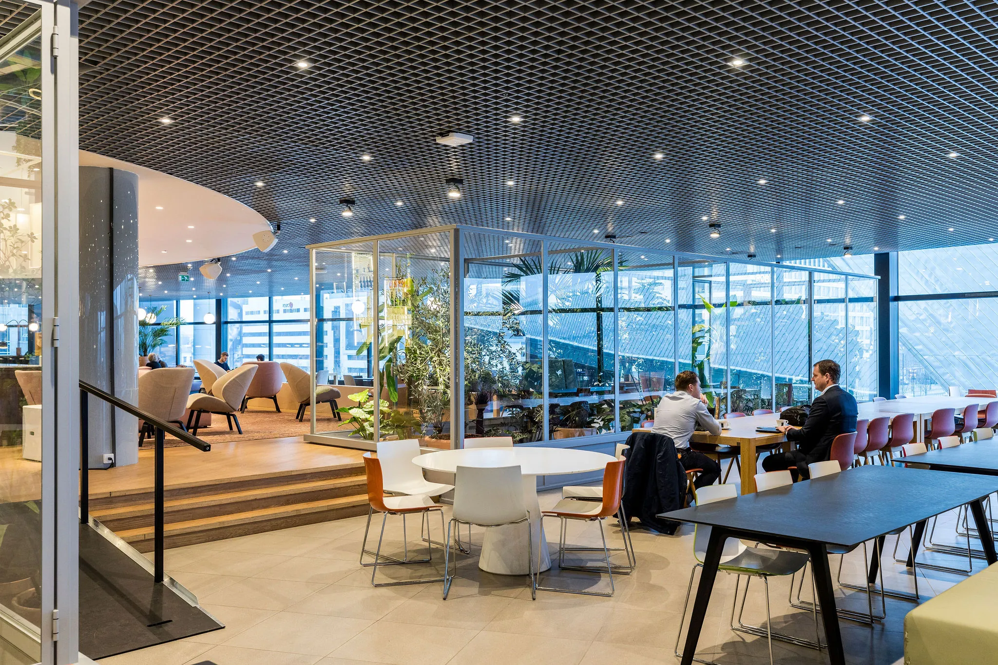 Moderne kantoorlounge aan het Weena met zitgedeeltes, vergadertafels en veel glas en planten.