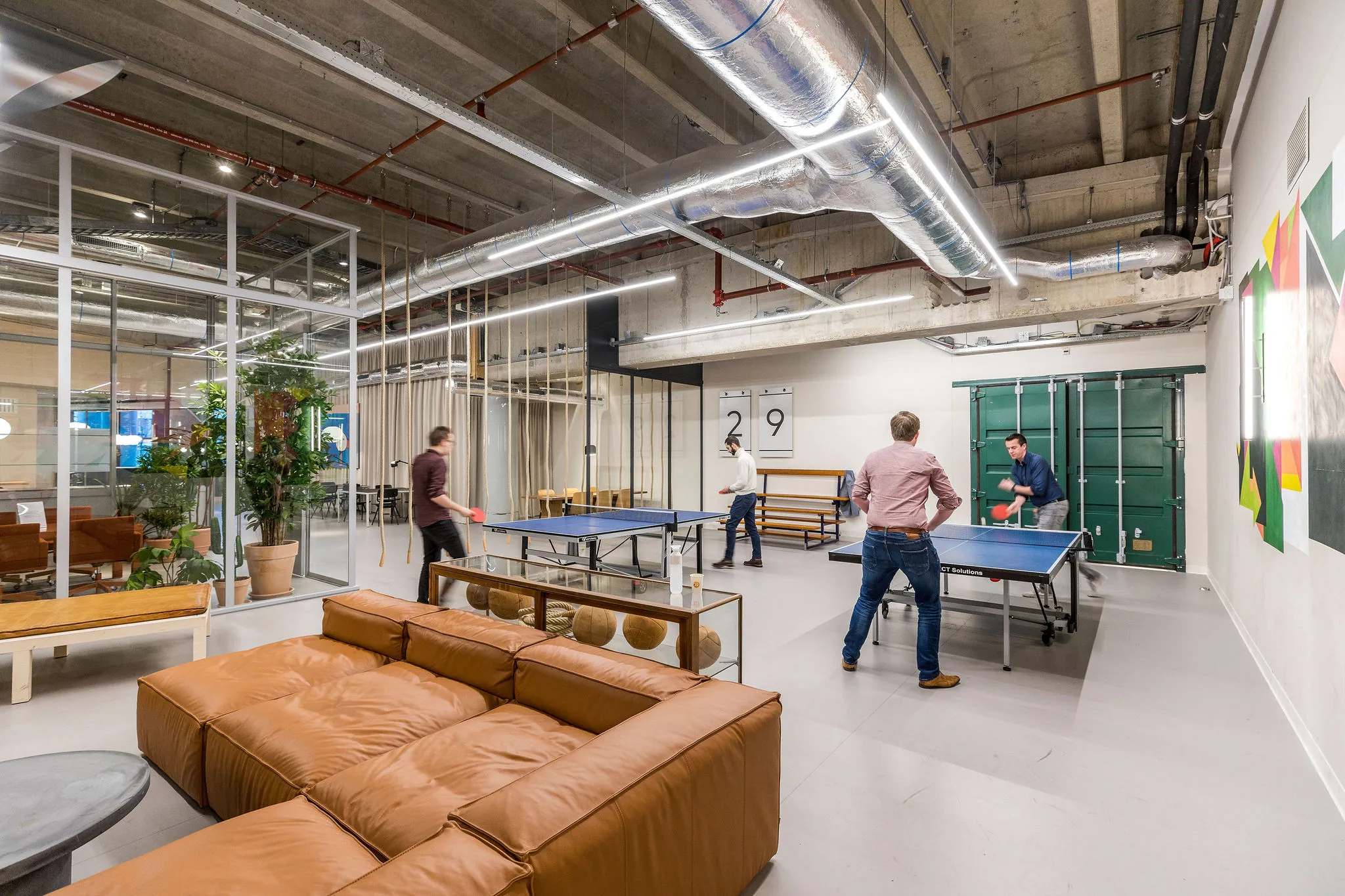 Vier mannen spelen tafeltennis in een moderne, industrieel ingerichte kantoorruimte aan het Weena.