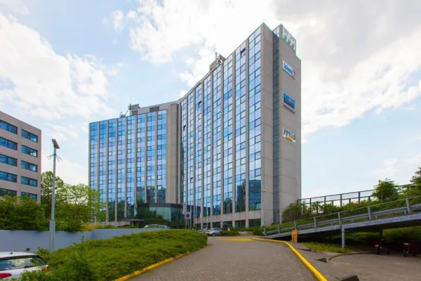 Een modern kantoorgebouw aan de Nevelgaarde met spiegelende ramen en meerdere bedrijfslogo’s op de gevel.