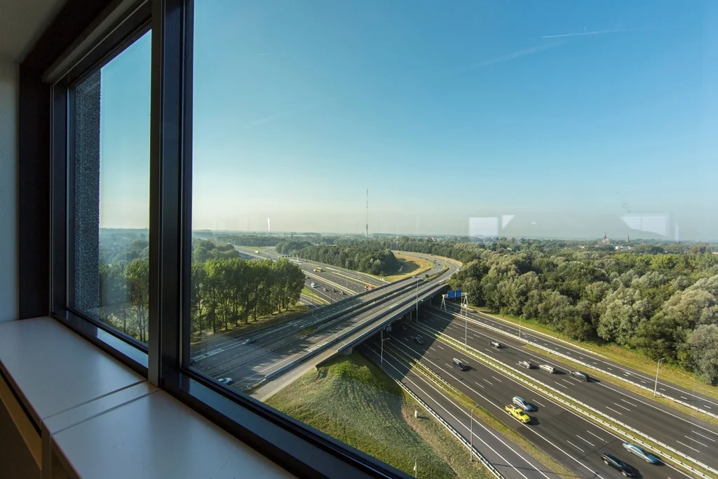 Uitzicht vanuit een raam op het knooppunt Nevelgaarde met snelwegen en omliggende groene omgeving.