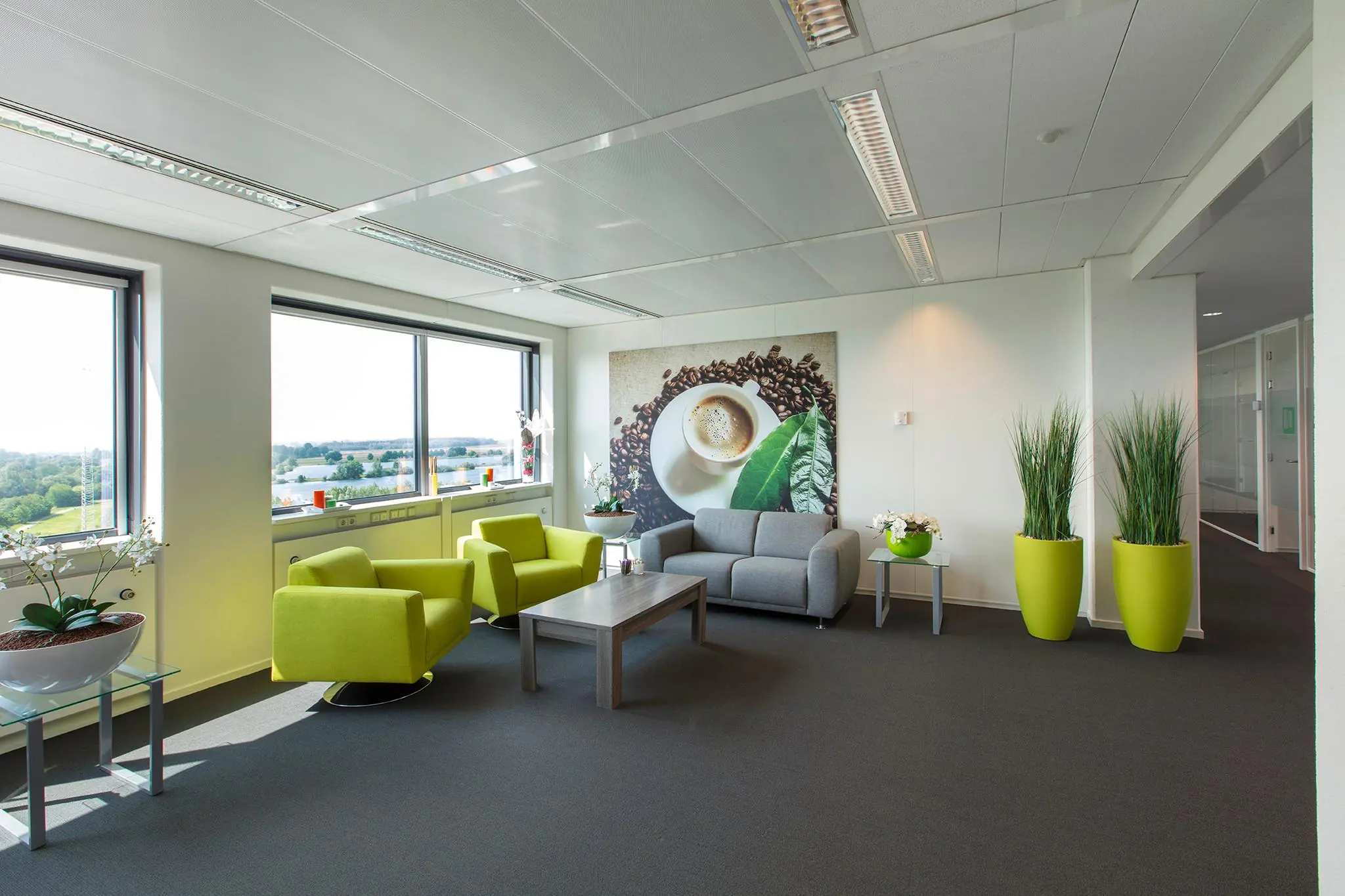 Moderne wachtruimte met felgroene stoelen, een grijze bank, veel planten en een grote koffiefoto aan de muur in kantoorgebouw Nevelgaarde.