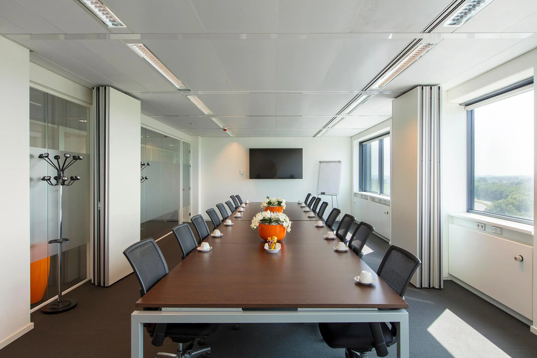 Vergaderruimte aan de Nevelgaarde met een lange tafel, moderne stoelen, grote ramen en een scherm aan de muur.
