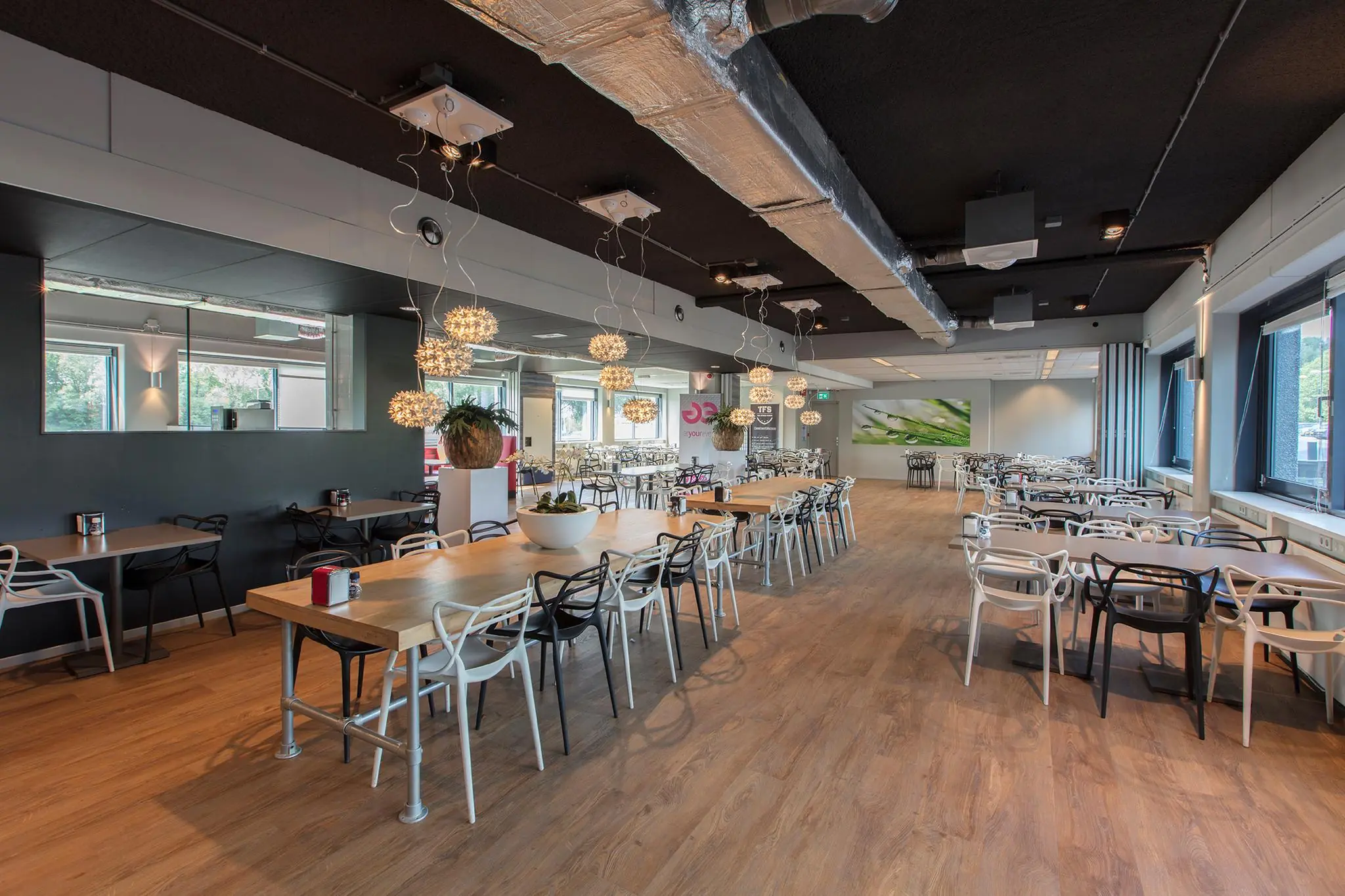 Modern ingerichte bedrijfs- of schoolkantine aan de Nevelgaarde met houten vloer, designstoelen en sfeervolle verlichting.