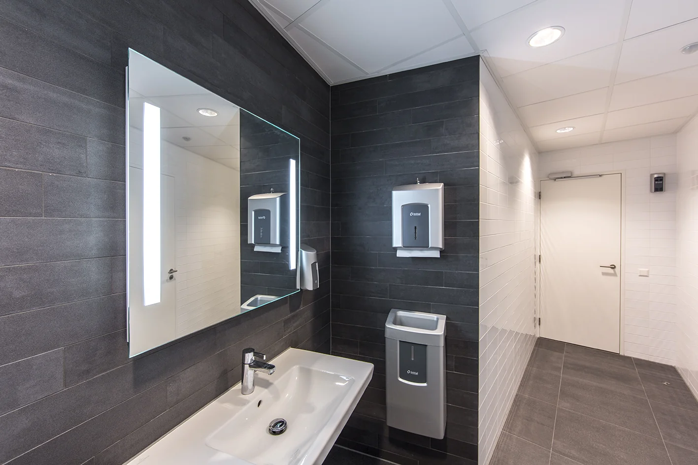 Moderne, nette toiletruimte met een wastafel, verlichte spiegel en wandgemonteerde hygiëneapparaten in Nevelgaarde.