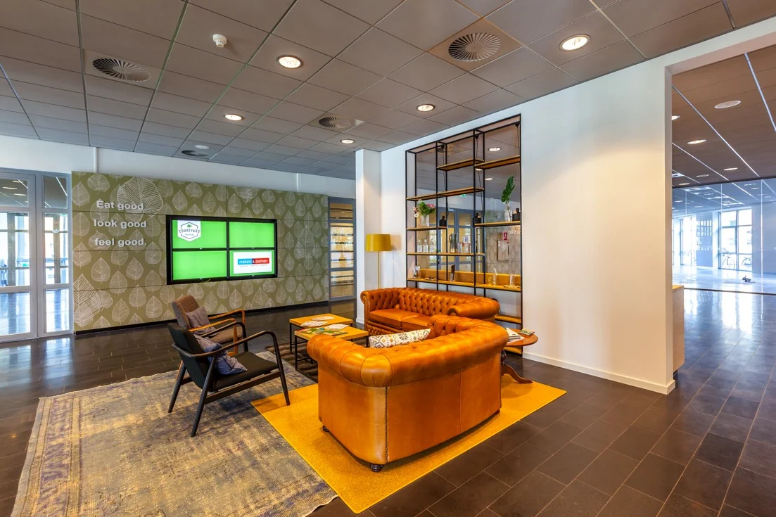 Moderne wachtruimte op Orteliuslaan met leren bank, decoratieve wand en digitale schermen.