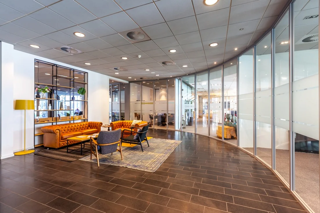 Moderne kantoorlobby aan de Orteliuslaan met glazen vergaderruimtes en een zithoek met leren banken.
