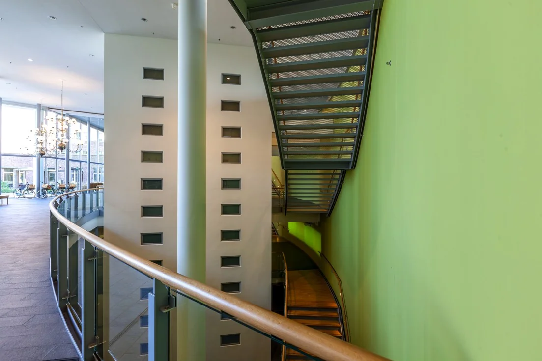 Moderne entreehal aan de Orteliuslaan met glazen balustrade, wenteltrap en felgroene muur.