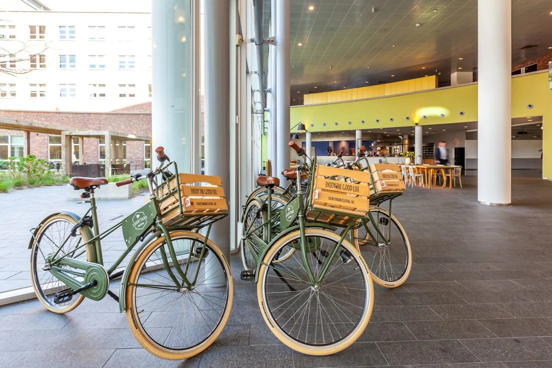 Groene vintage fietsen met houten kratjes staan opgesteld in de lobby van een modern kantoorgebouw aan de Orteliuslaan.