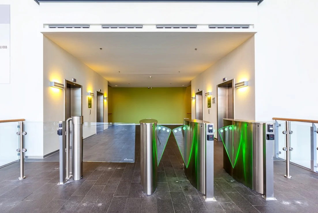 Ingang met elektronische toegangspoortjes en vier liften in een modern kantoorgebouw aan de Orteliuslaan.