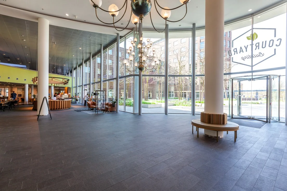Ruime en moderne entreehal van het kantoorpand aan de Orteliuslaan, met grote raampartijen, een zitgedeelte en een koffiebar.