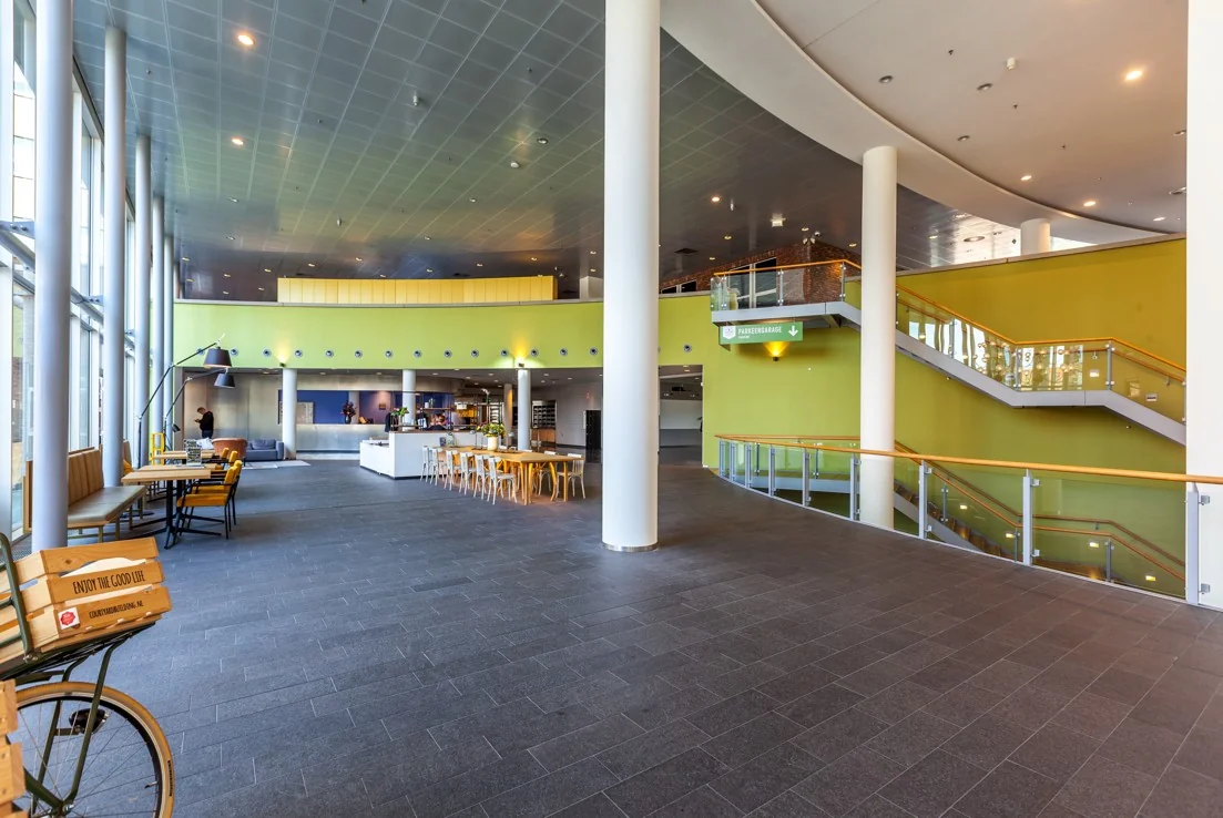 Ruime, moderne entreehal aan de Orteliuslaan met een zithoek, koffiebar en trap naar de parkeergarage.