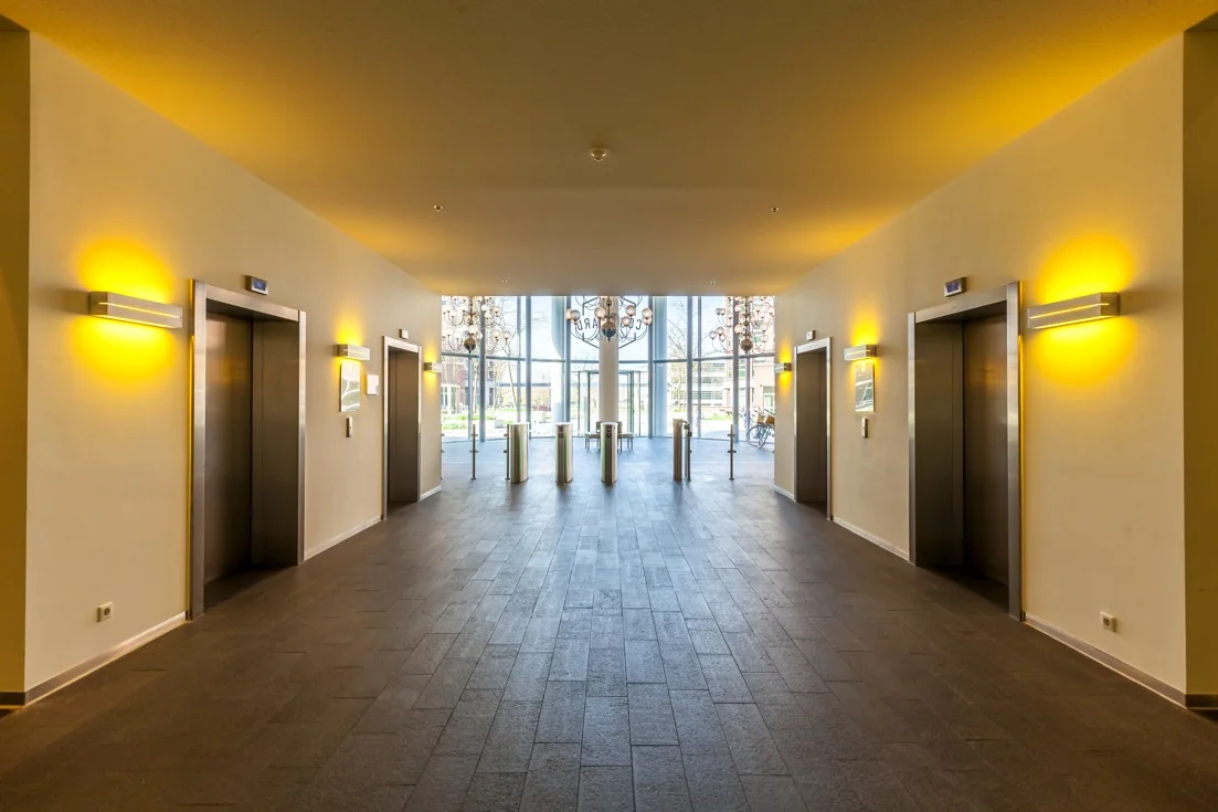 Modern ingerichte entreehal met vier liften, toegangspoortjes en grote glazen gevel aan de Orteliuslaan.