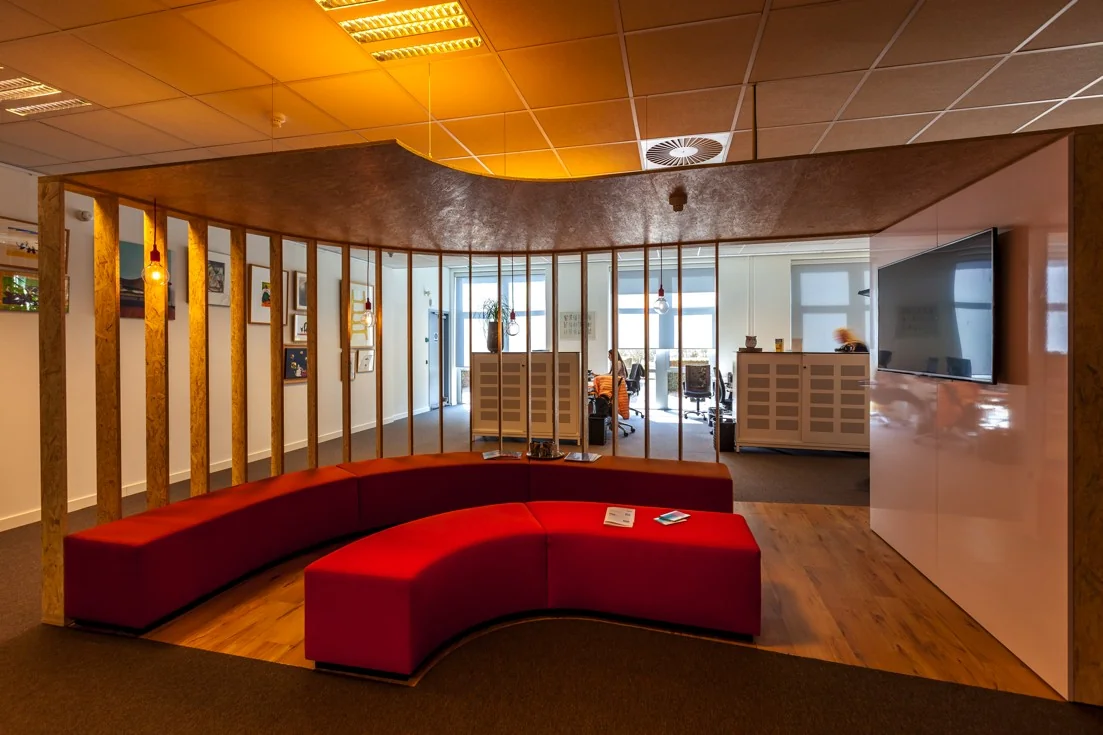 Moderne kantoorruimte aan de Orteliuslaan met een rode gebogen zitbank, houten lamellenwand en zicht op werkplekken.
