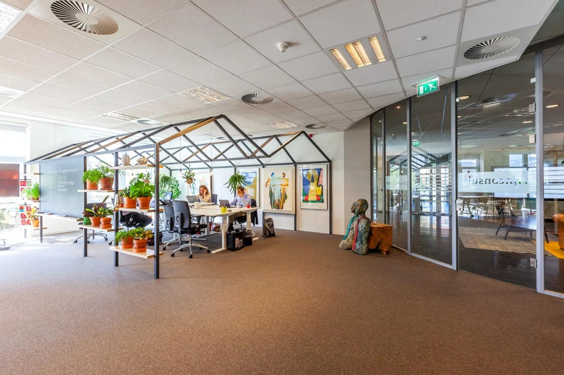 Open kantoorruimte aan de Orteliuslaan met een huisvormige werkconstructie, veel planten en moderne kunst aan de muur.