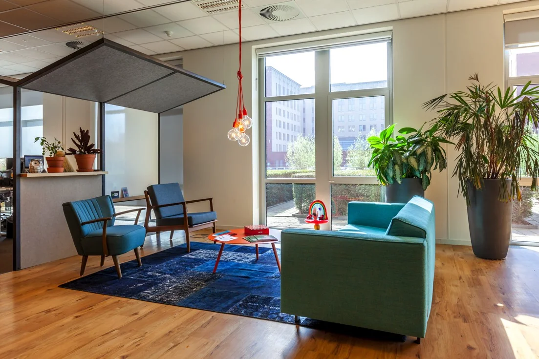 Moderne wachtruimte aan de Orteliuslaan met turquoise meubilair, grote planten en veel natuurlijk licht.