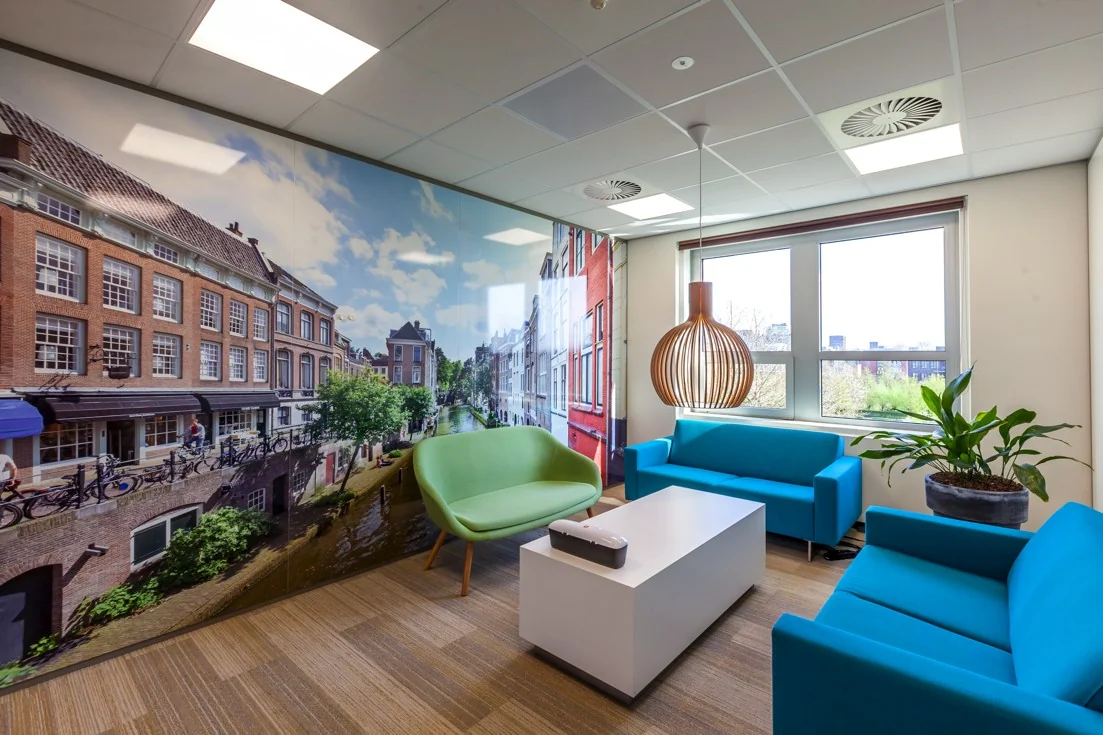 Moderne wachtruimte met felgekleurde banken, een grote fotowand van een Nederlandse grachtenstraat en veel natuurlijk licht.