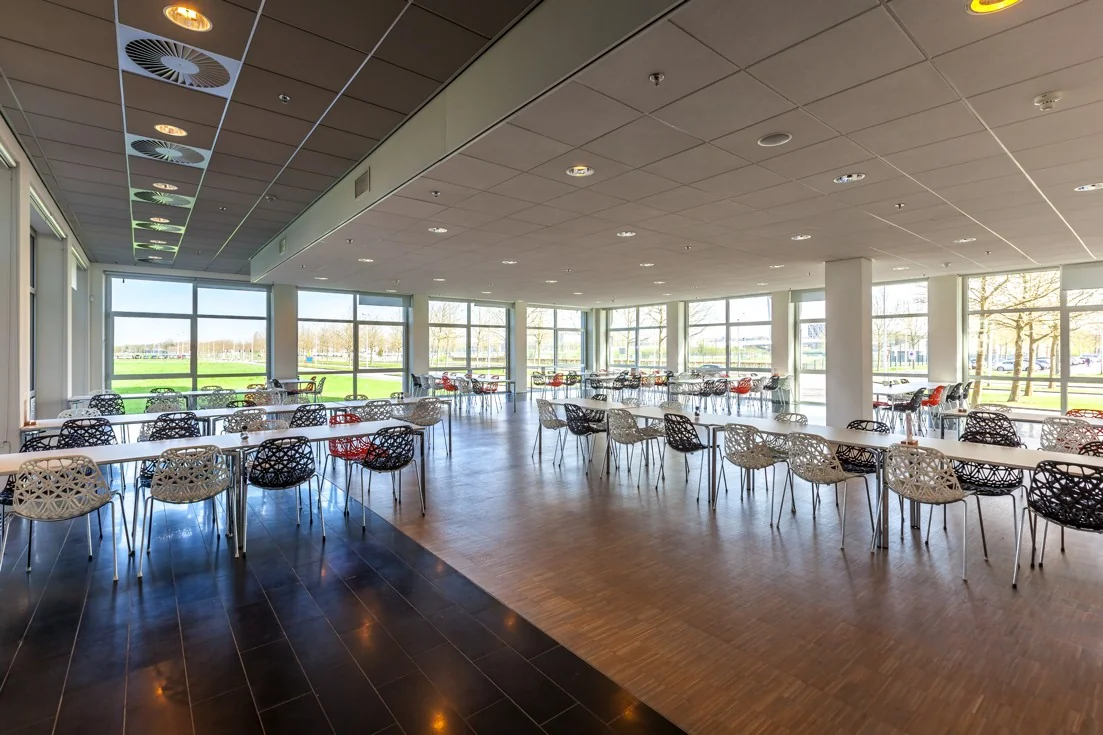 Ruime en lichte bedrijfskantine aan de Orteliuslaan met moderne stoelen en grote ramen met uitzicht op het groen.