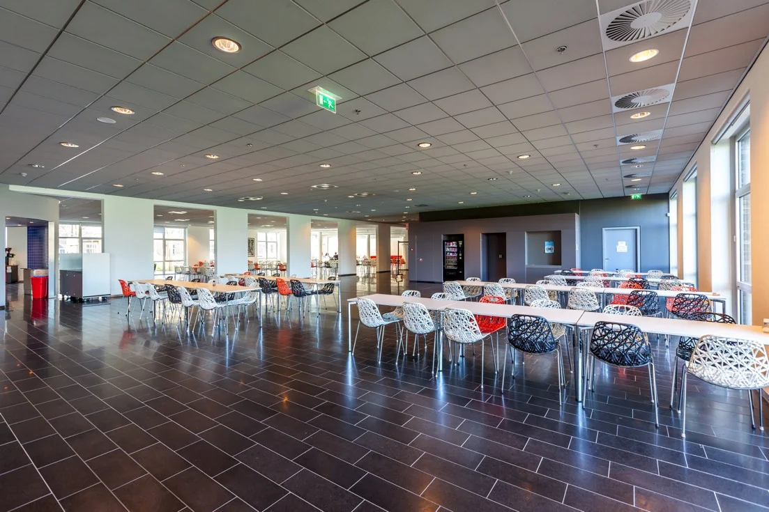 Moderne, ruime bedrijfskantine met kleurrijke stoelen en lange tafels aan de Orteliuslaan.