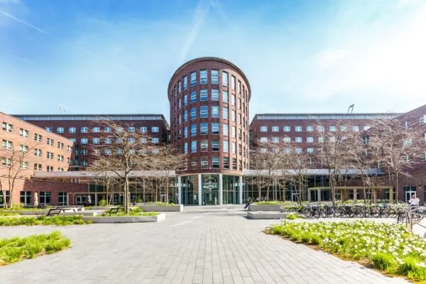 Vooraanzicht van het Courtyard-gebouw aan de Orteliuslaan in Utrecht, met bakstenen gevel en bloemperken op de voorgrond.