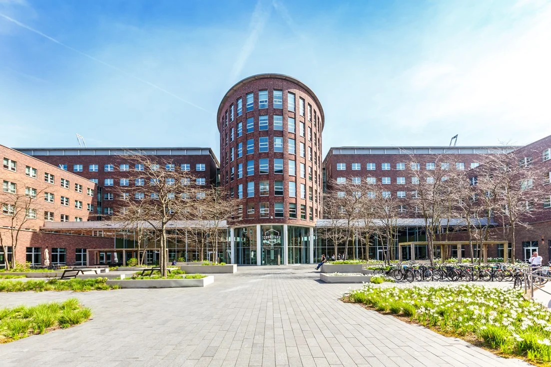 Vooraanzicht van het Courtyard-gebouw aan de Orteliuslaan in Utrecht, met bakstenen gevel en bloemperken op de voorgrond.
