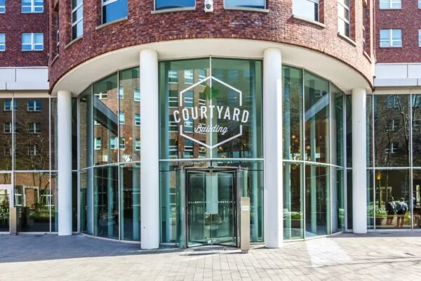 Glazen entree van het Courtyard Building aan de Orteliuslaan met ronde gevel en witte zuilen.