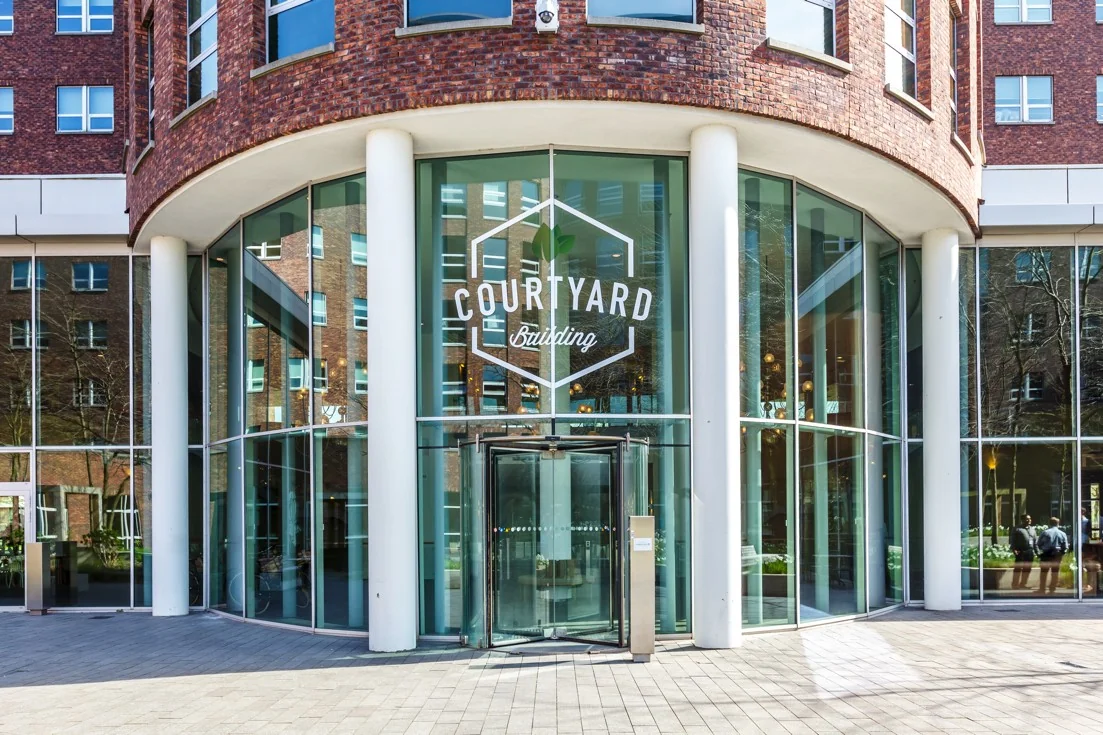 Glazen entree van het Courtyard Building aan de Orteliuslaan met ronde gevel en witte zuilen.