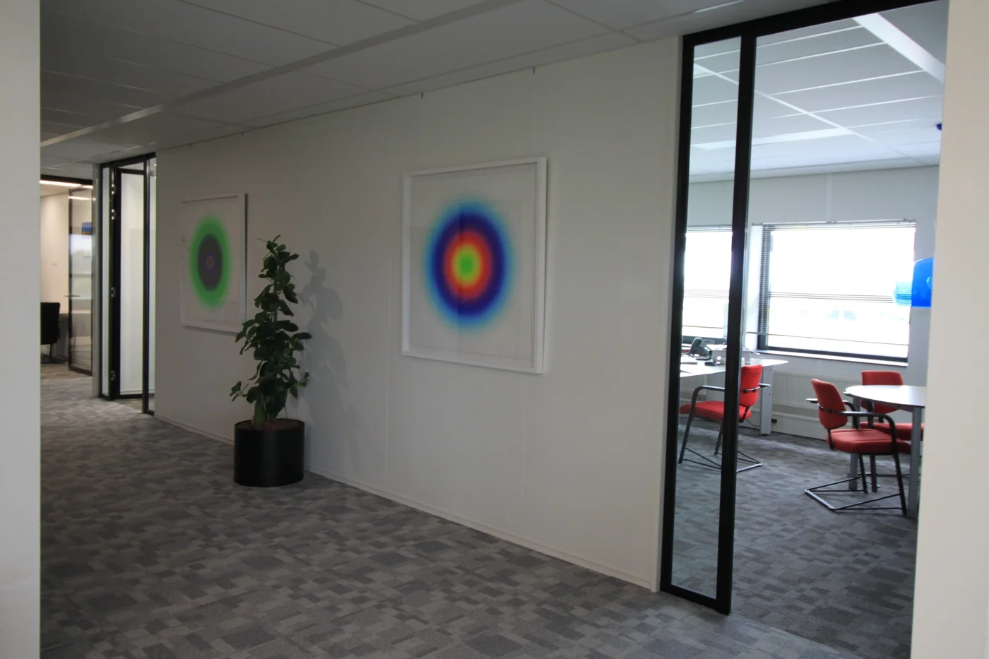 Kantoorruimte aan de Marconibaan met moderne inrichting, kleurrijke kunst aan de muur en zicht op een vergaderruimte met rode stoelen.