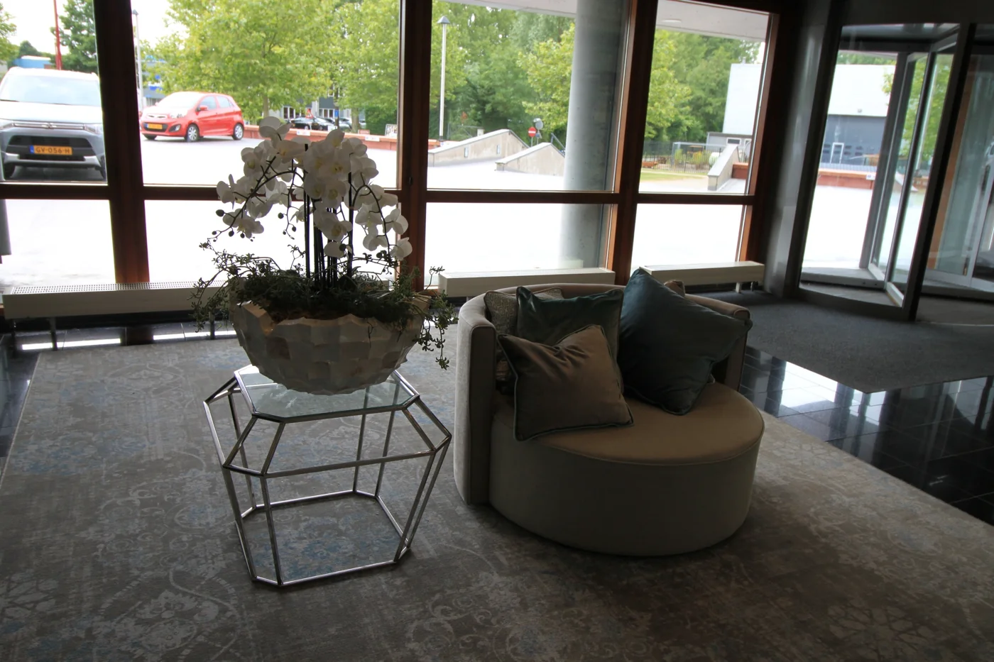 Zitgelegenheid met sierkussen en bloempot met witte orchideeën in de lobby aan de Marconibaan.