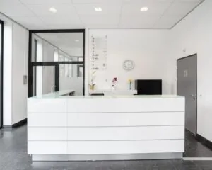 Moderne witte receptiebalie in een strak en licht kantoorinterieur met bloemen en een wandklok.