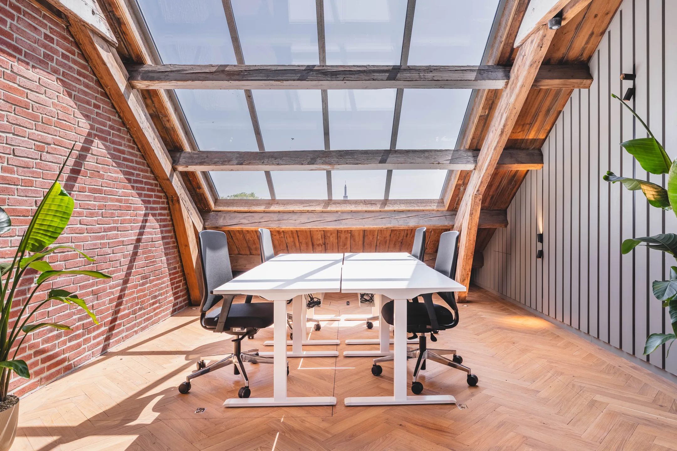 Een moderne kantoorruimte met bakstenen muur en groot dakraam boven twee bureaus en stoelen.