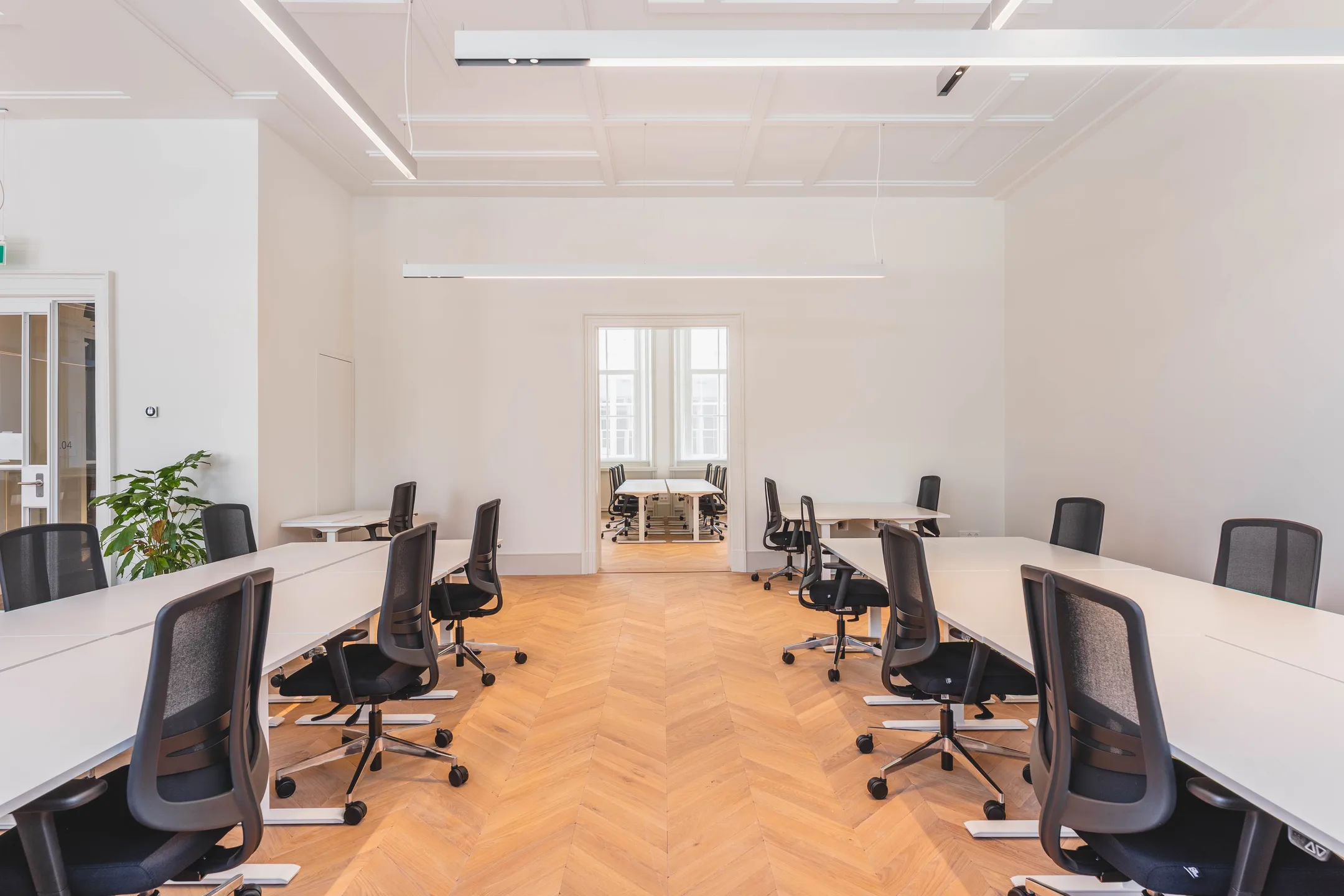 Ruime, moderne kantoorruimte met lange tafels en zwarte stoelen.