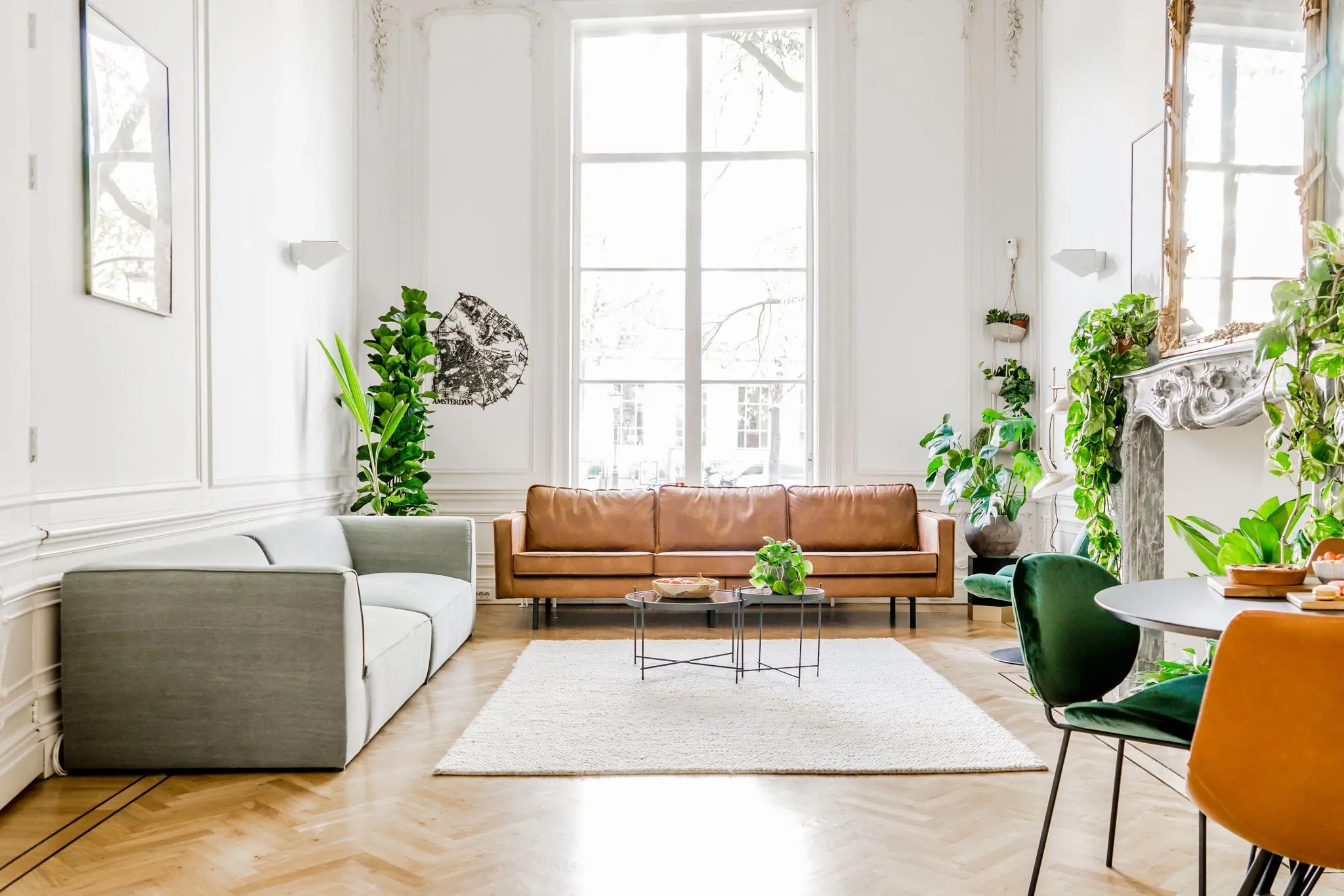 Stijlvol ingerichte woonkamer aan de Herengracht met hoge ramen, moderne meubels en veel groene planten.