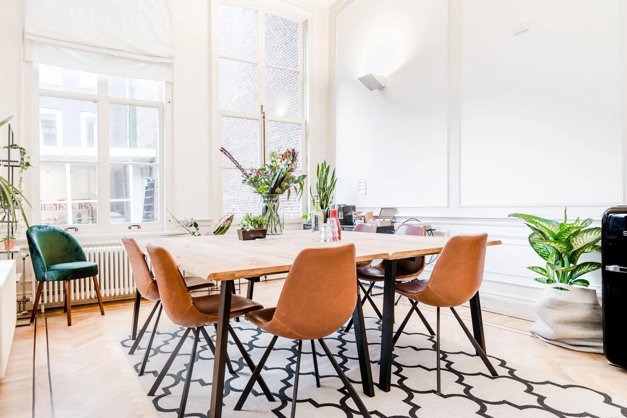 Stijlvol vergaderruimte-interieur aan de Herengracht met houten tafel, leren stoelen, grote ramen en groene planten.