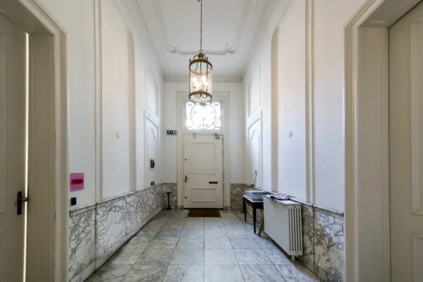 Lichte marmeren hal in een grachtenpand aan de Herengracht met hoge plafonds, klassieke deuren en een hangende lantaarnlamp.