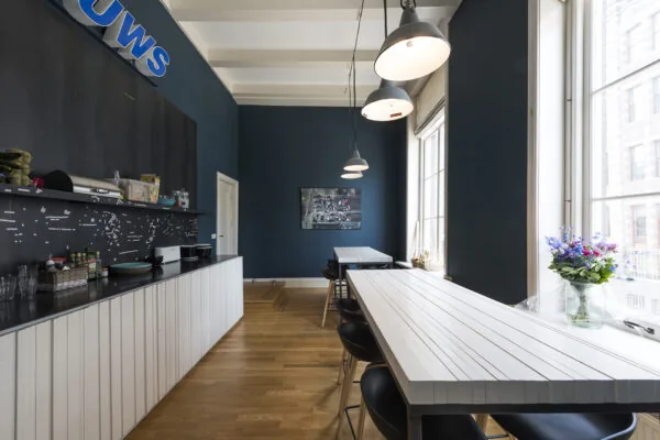 Moderne kantineruimte aan de Herengracht met hoge ramen, blauwe muren en lange witte tafels.