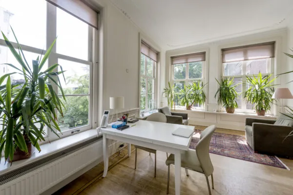 Licht en modern kantoor aan de Herengracht met grote ramen, groene planten en een wit bureau.
