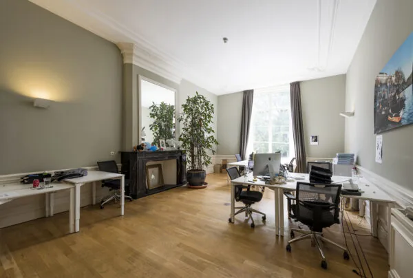 Modern ingericht kantoorpand aan de Herengracht met hoge plafonds, houten vloer, grote raampartij en meerdere werkplekken.