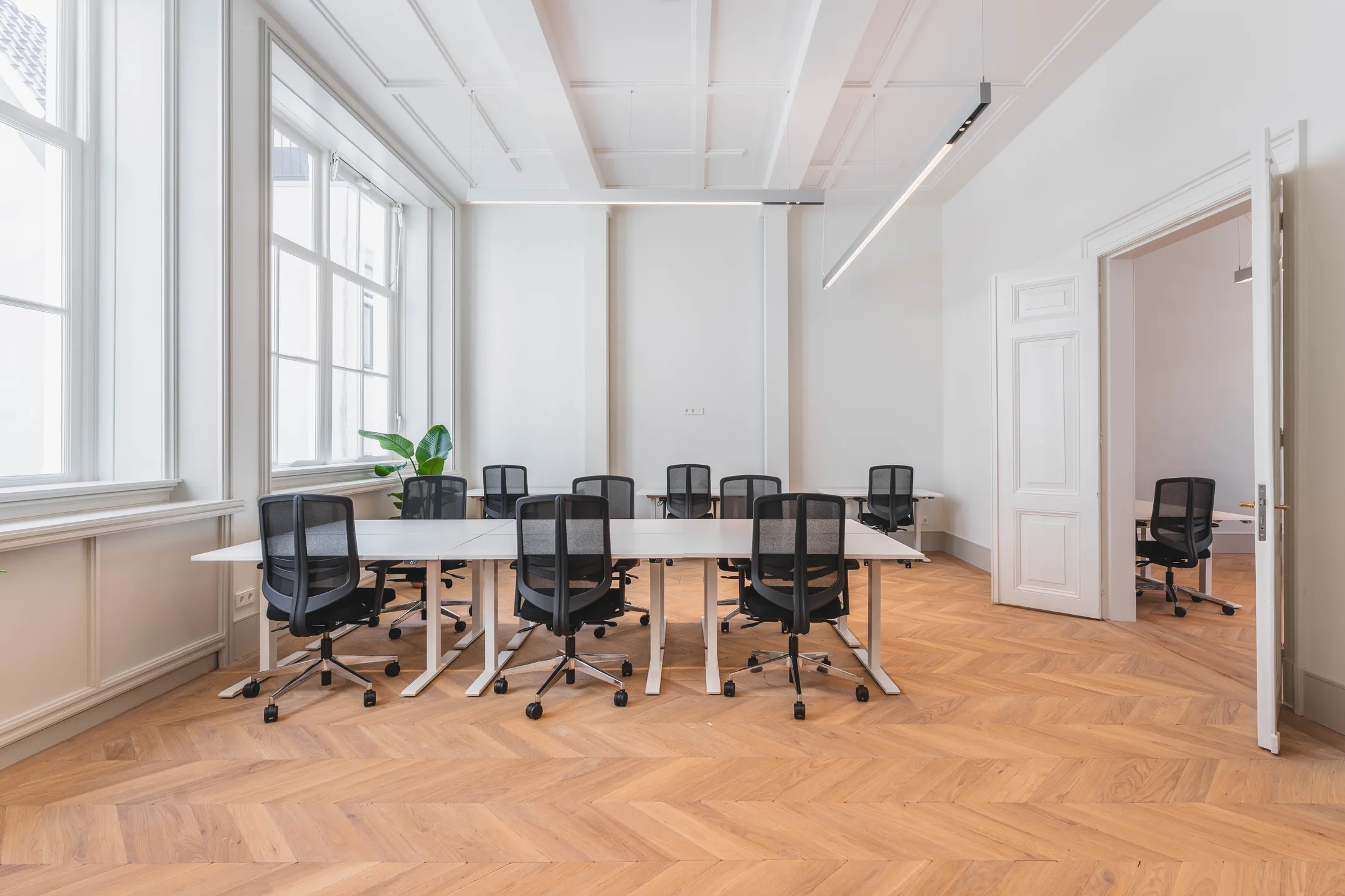 Een moderne vergaderruimte met zwarte stoelen en witte tafels op een visgraat houten vloer.