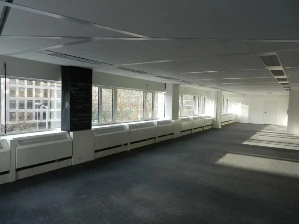 Lichte, lege kantoorruimte aan de Westblaak met grote ramen en grijze vloerbedekking.