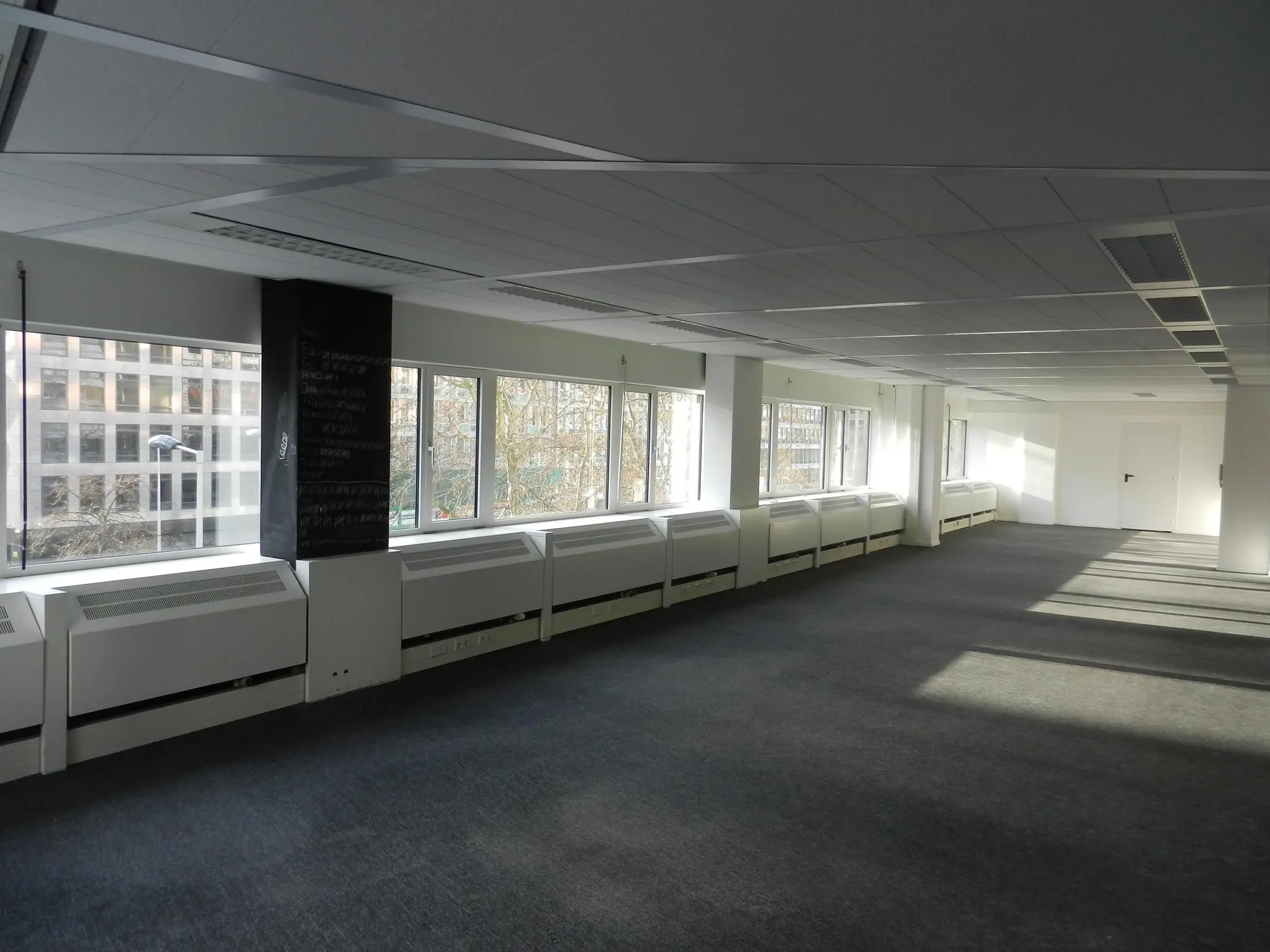 Lichte, lege kantoorruimte aan de Westblaak met grote ramen en grijze vloerbedekking.