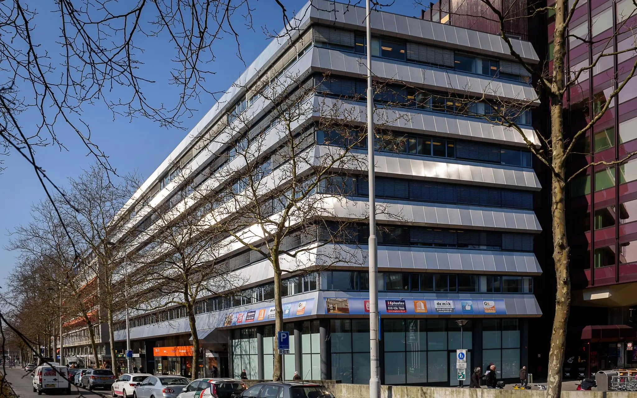 Kantoorpand aan de Westblaak in Rotterdam met winkels op de begane grond en geparkeerde auto's langs de straat.