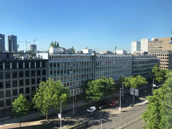 Kantoorgebouwen aan de Westblaak in Rotterdam met op de voorgrond een brede straat en groene bomen.