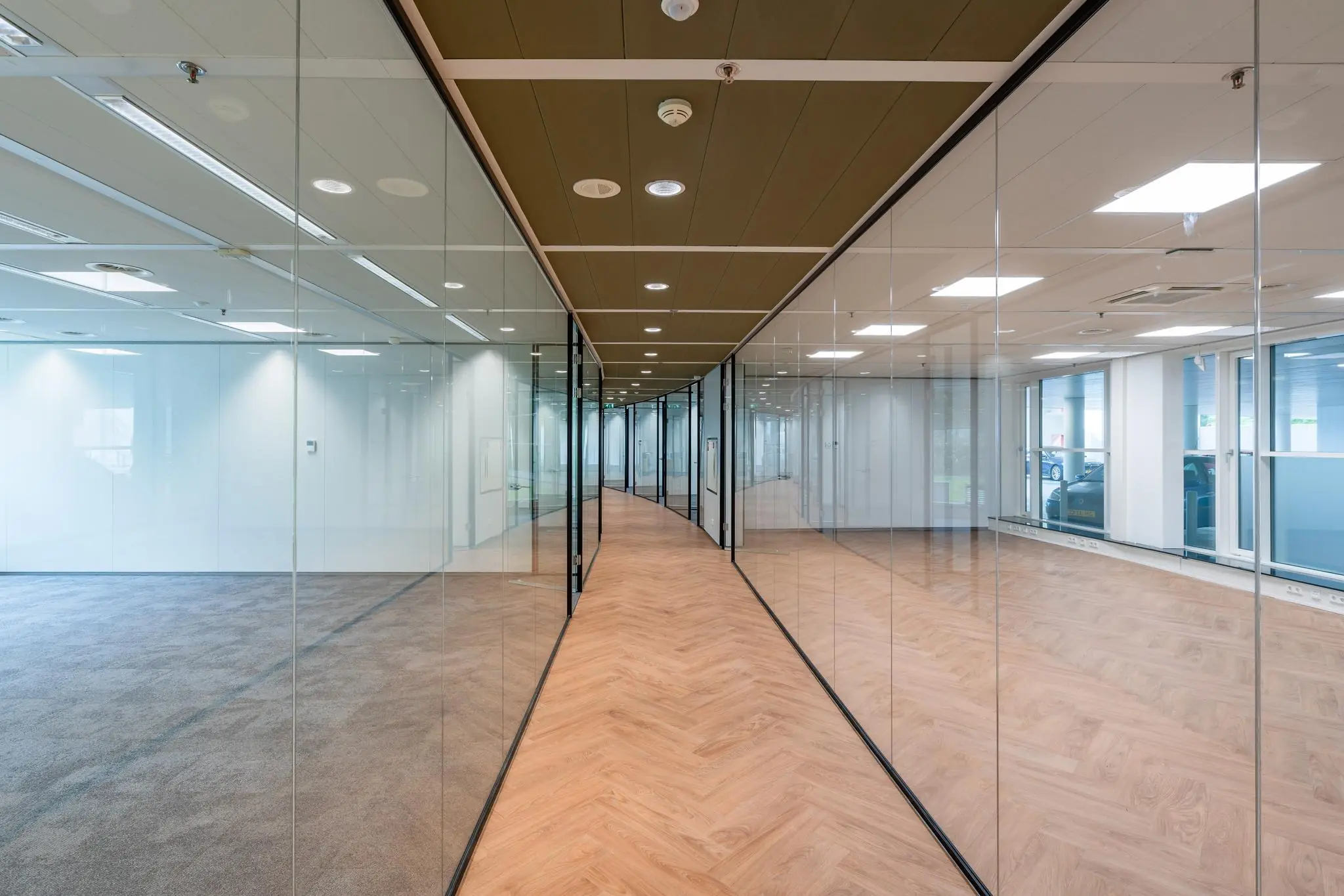 Gang met glazen wanden en houten visgraatvloer in een modern kantoorgebouw aan de Newtonlaan.