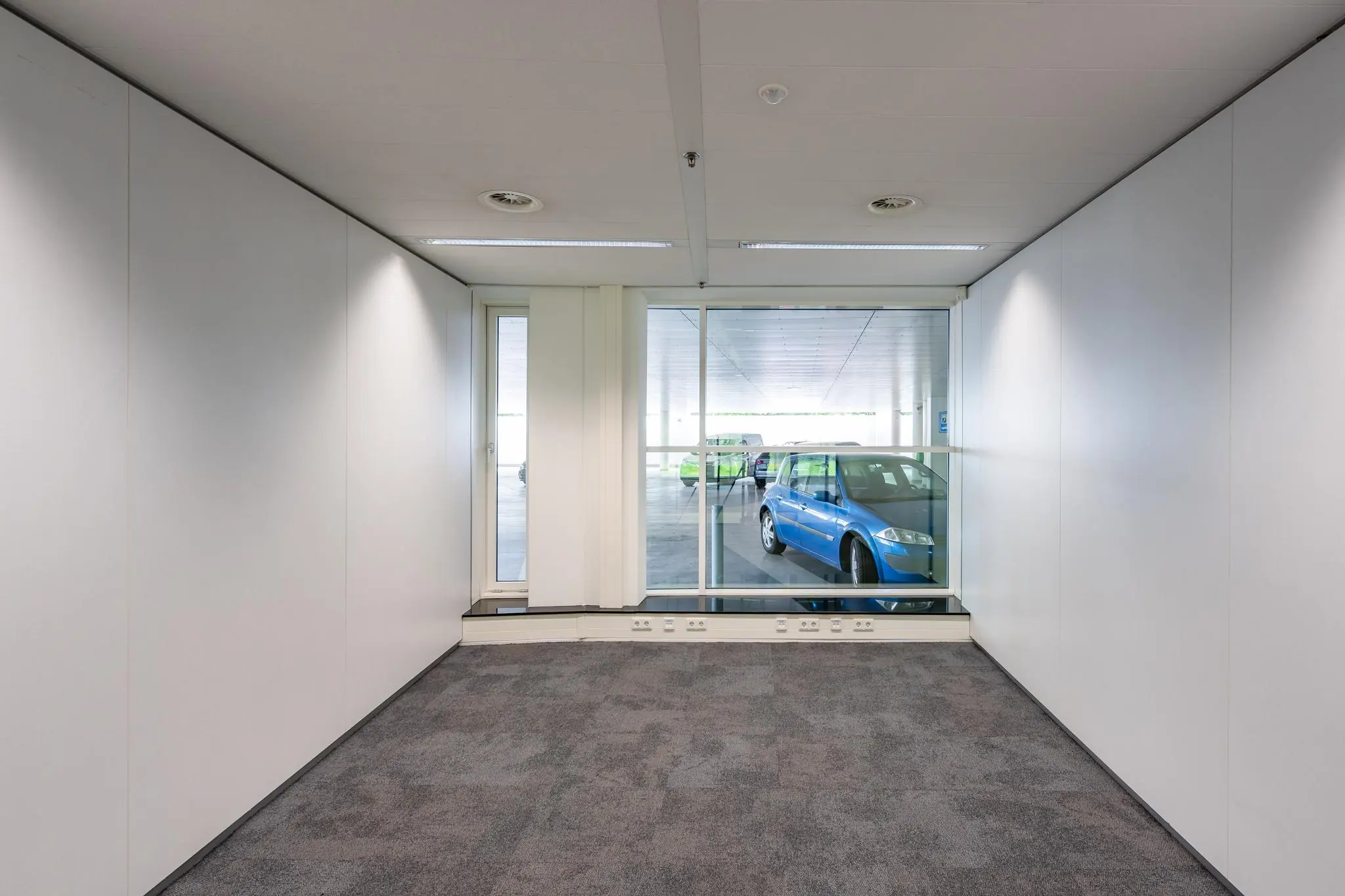 Lege kantoorruimte aan de Newtonlaan met uitzicht op een parkeergarage en een geparkeerde blauwe auto.