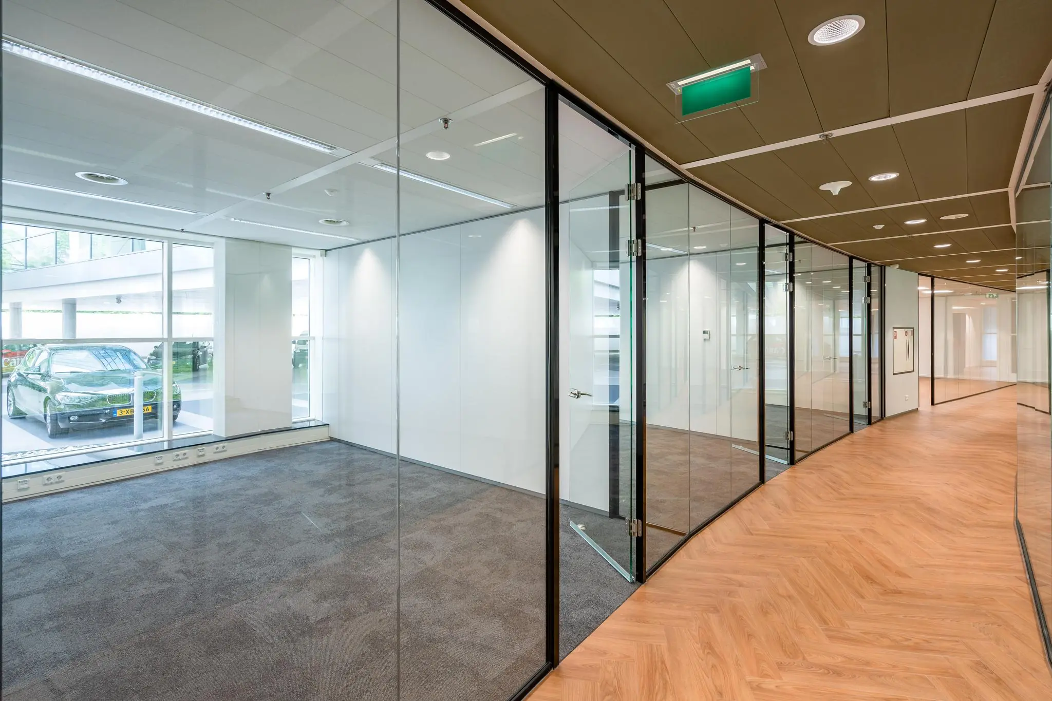 Moderne kantoorruimte in het Newtonlaan-gebouw met glazen wanden, houten vloer en uitzicht op een geparkeerde auto buiten.