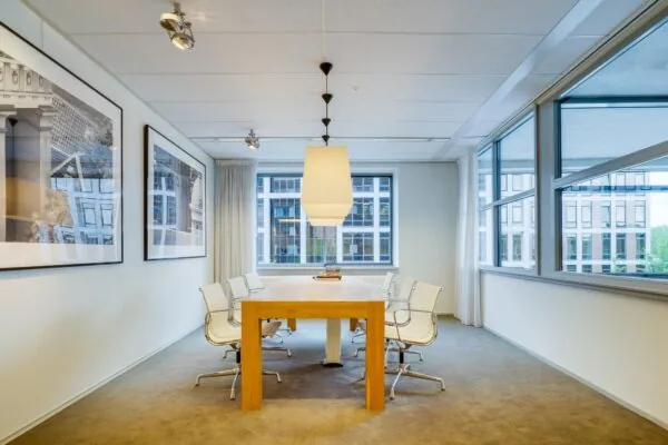 Vergaderruimte aan de Euclideslaan met een houten tafel, witte stoelen en grote ramen met uitzicht op kantoorgebouwen.