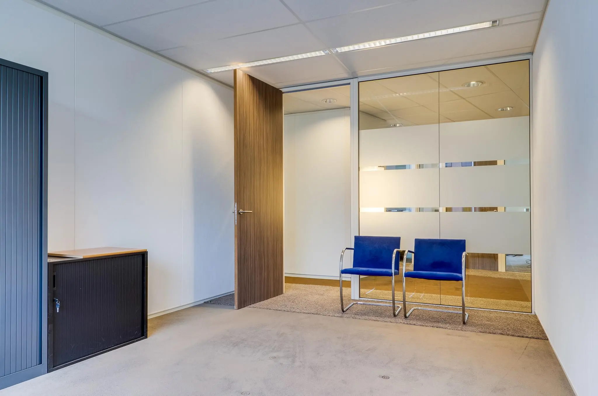 Wachtruimte met twee blauwe stoelen, een houten deur en glazen wand in een kantoorpand aan de Euclideslaan.