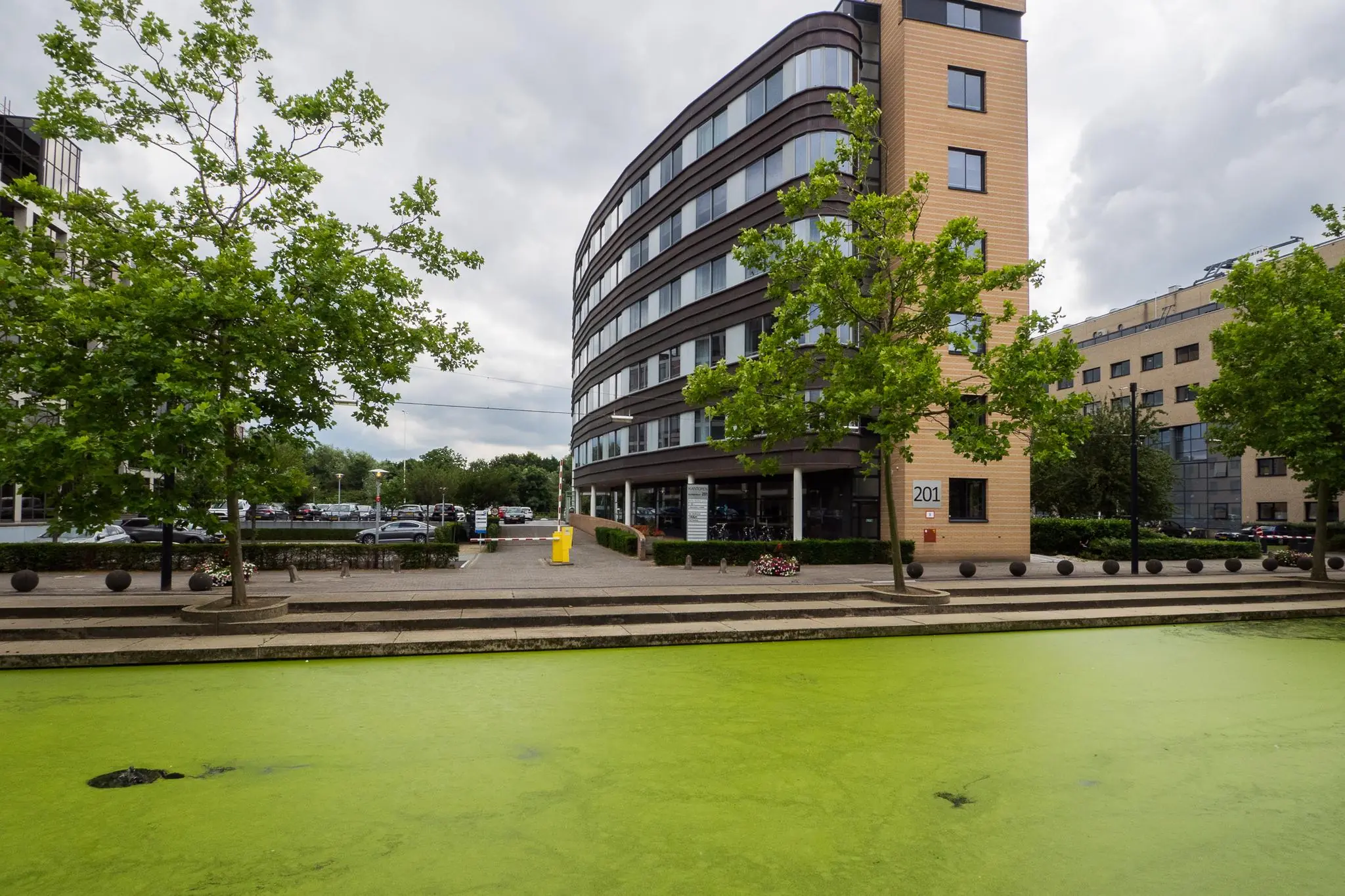 Kantoorgebouw aan de Euclideslaan 201 met vijver op de voorgrond en bomen langs het pad.