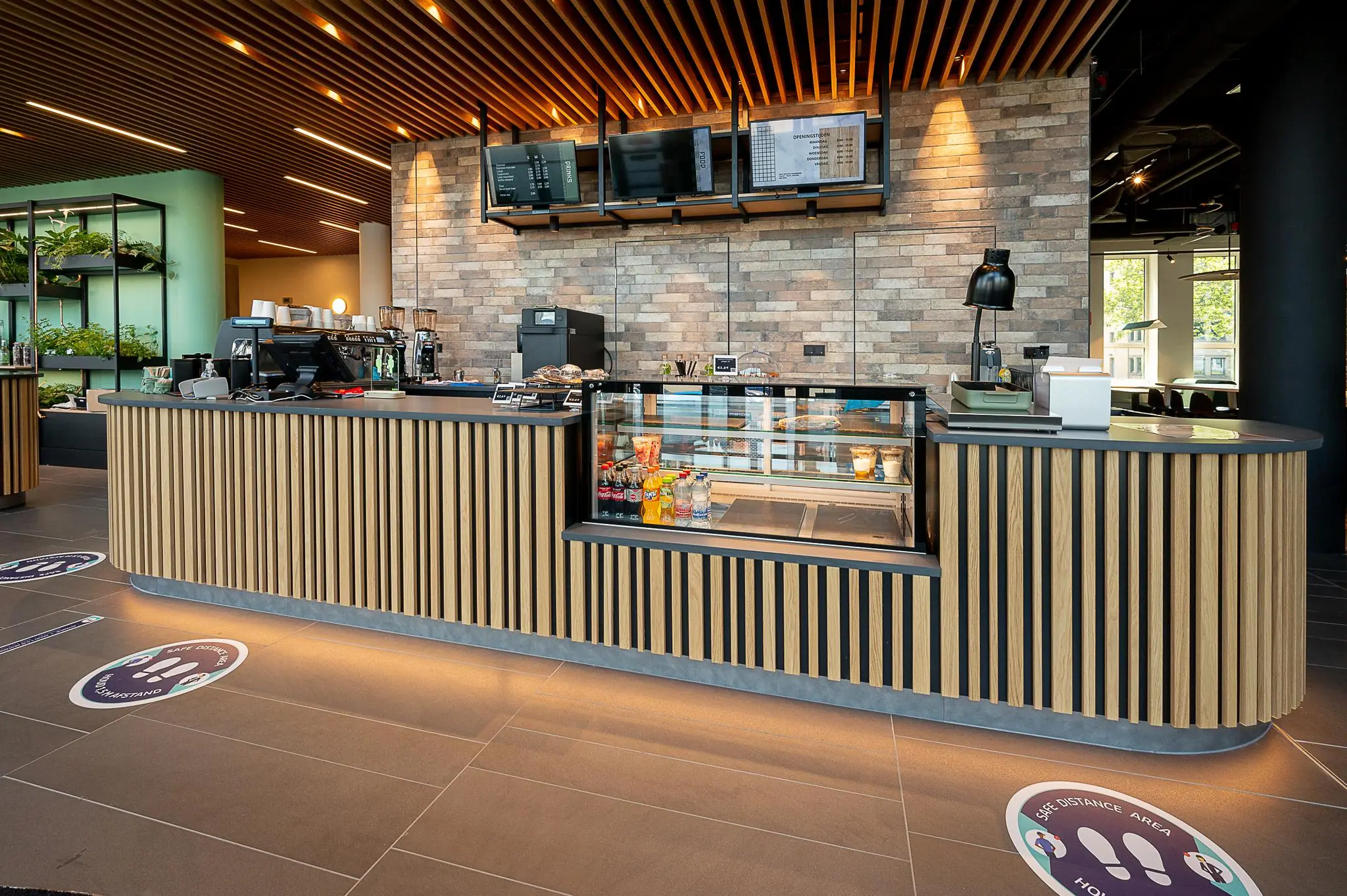 Moderne koffiebar met houten balie, koelvitrine en digitale menuborden aan de Watermanweg.