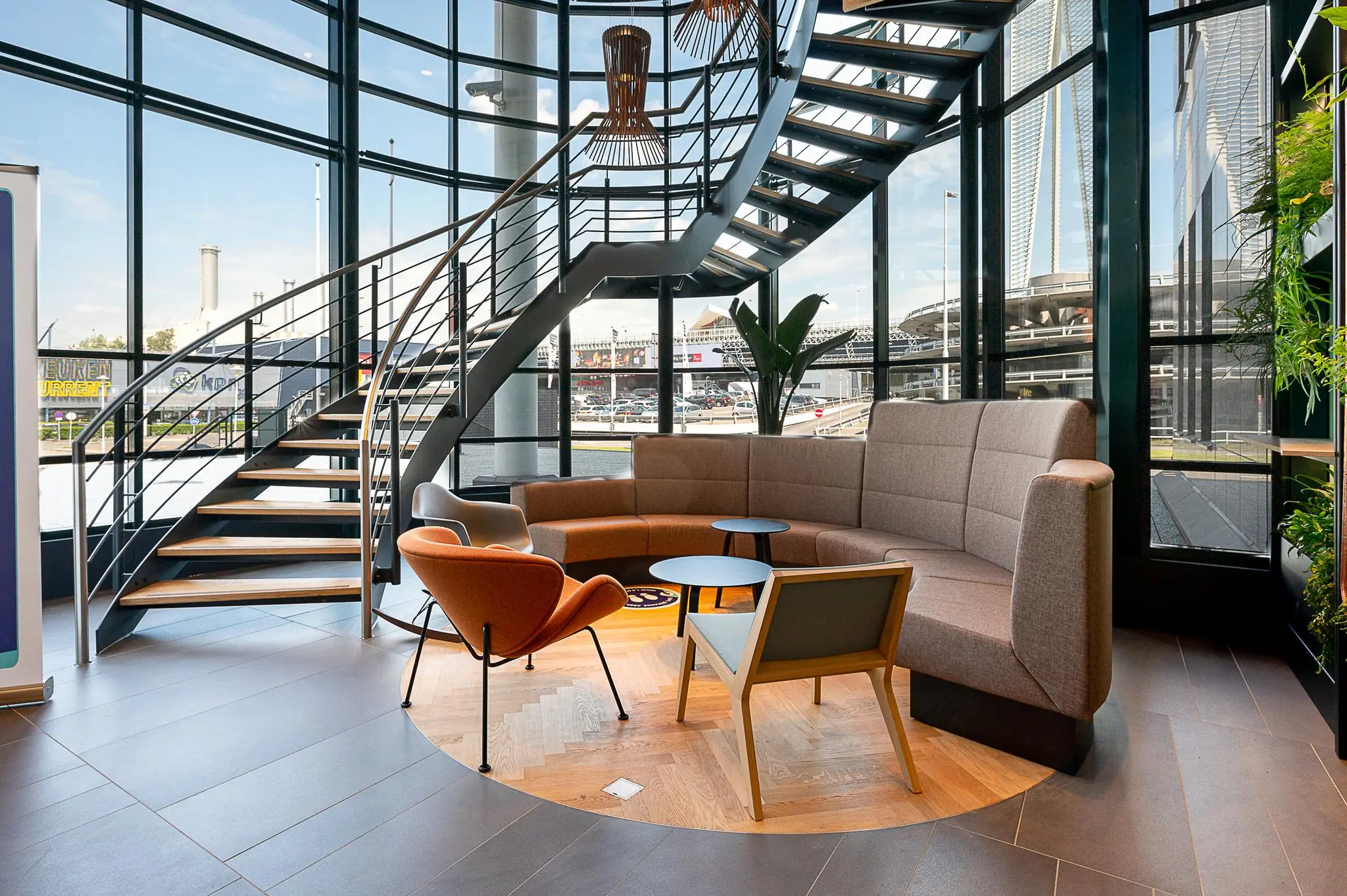 Moderne wachtruimte met ronde zitbank, designstoelen en wenteltrap in een glazen gebouw aan de Watermanweg.